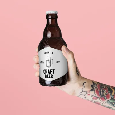 Tattooed arm holding a brown glass bottle psd mockup